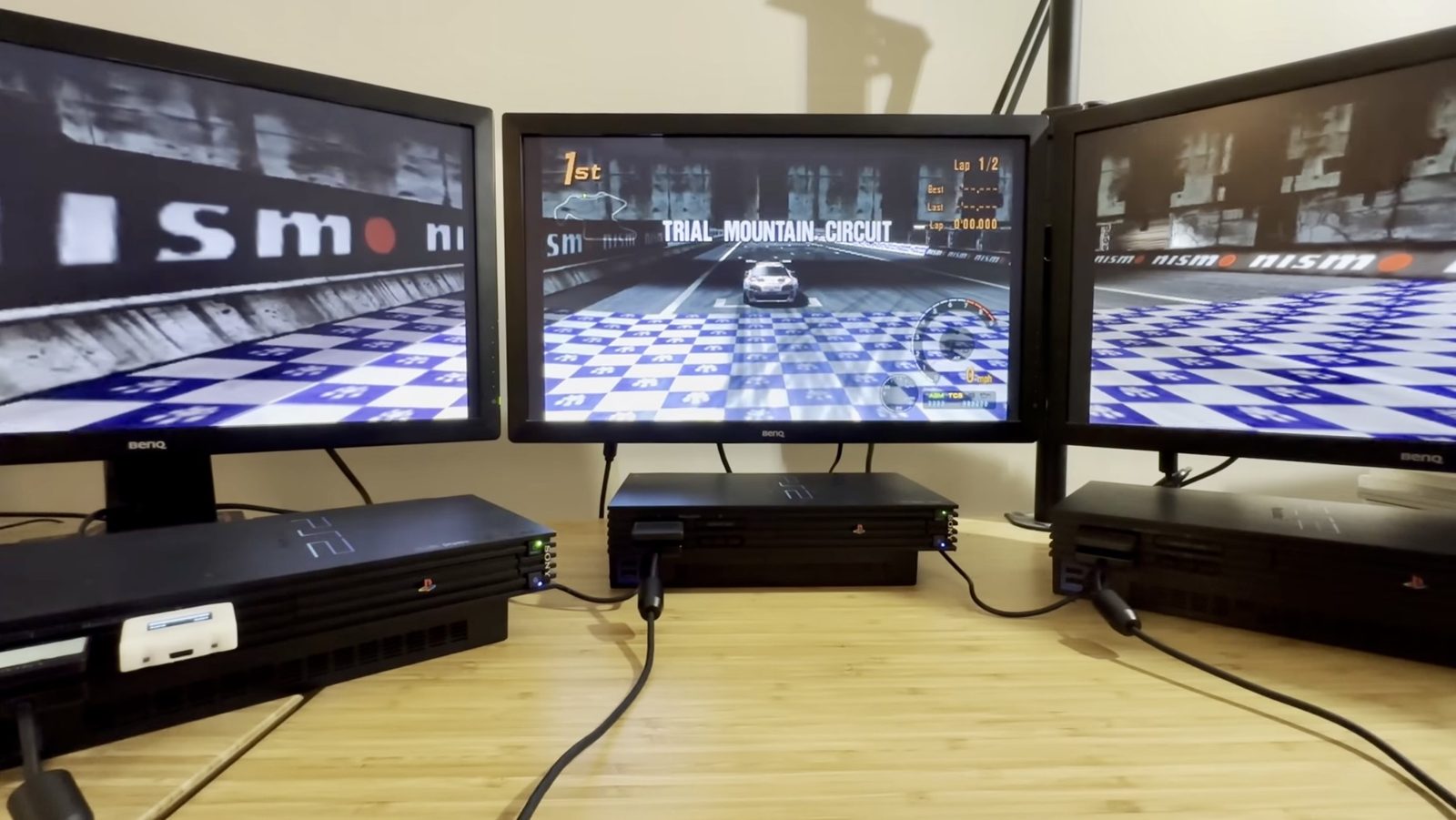 Trial Mountain's checkered starting grid, correctly synced across all three screens — the NISMO ad boards line up on both sides